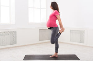 Pregnant woman stretching with some light yoga at home