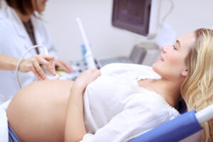 Happy pregnant female visiting women's doctor in the maternity center, doing ultrasound scan, worried about the health of the child