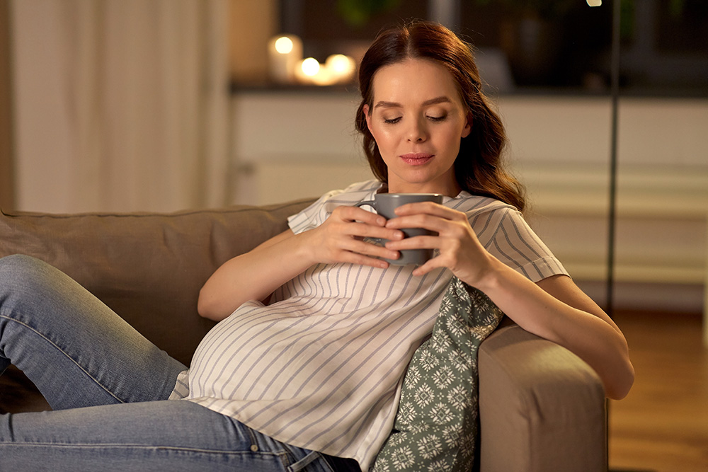 Pregnant woman resting on a sofa with a cup of tea